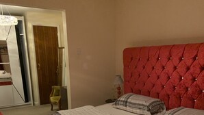 A neatly made bed with a plaid bedspread and pillows, a red upholstered headboard, and a red bench at the foot of the bed. - Beautiful big Independent Furnished Bungalow (High Wycombe)