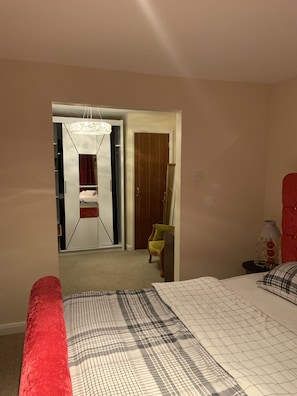 A bedroom with a bed, a red chair, a wooden wardrobe, and a mirror. - Beautiful big Independent Furnished Bungalow (High Wycombe)