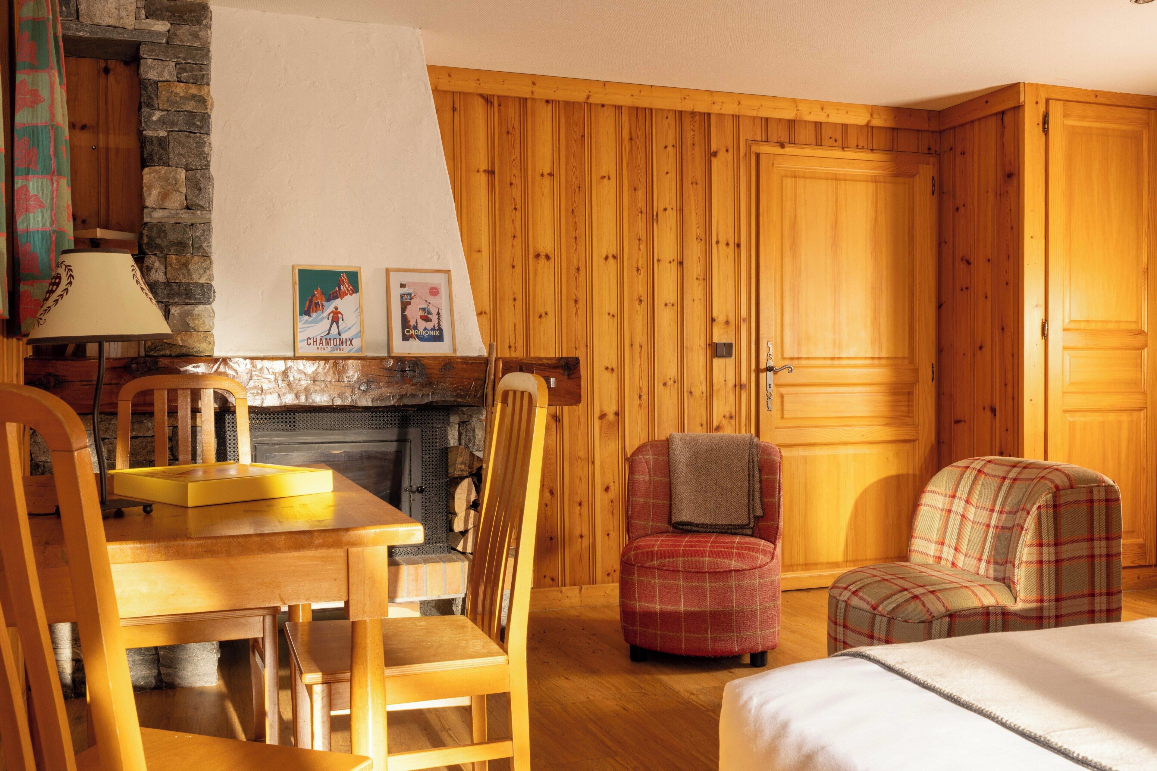 A cozy room with wooden walls, a fireplace, a dining table with chairs, and a plaid armchair.