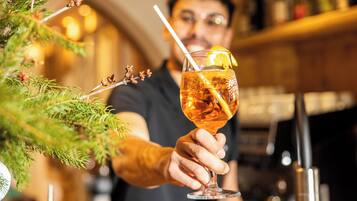 Eine Person hält ein Glas mit Strohhalm und Zitronenscheibe, unscharfer Hintergrund lässt eine Bar oder ein Restaurant vermuten.