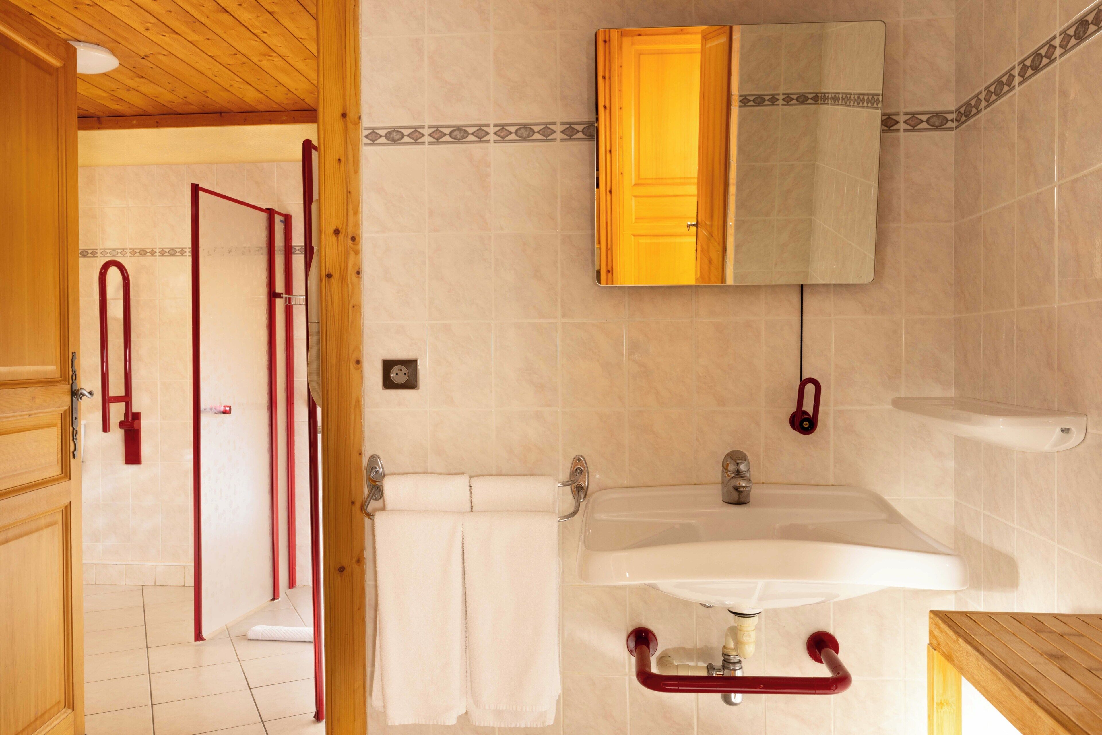 A bathroom with a wooden door, a sink, a mirror, and a shower area.