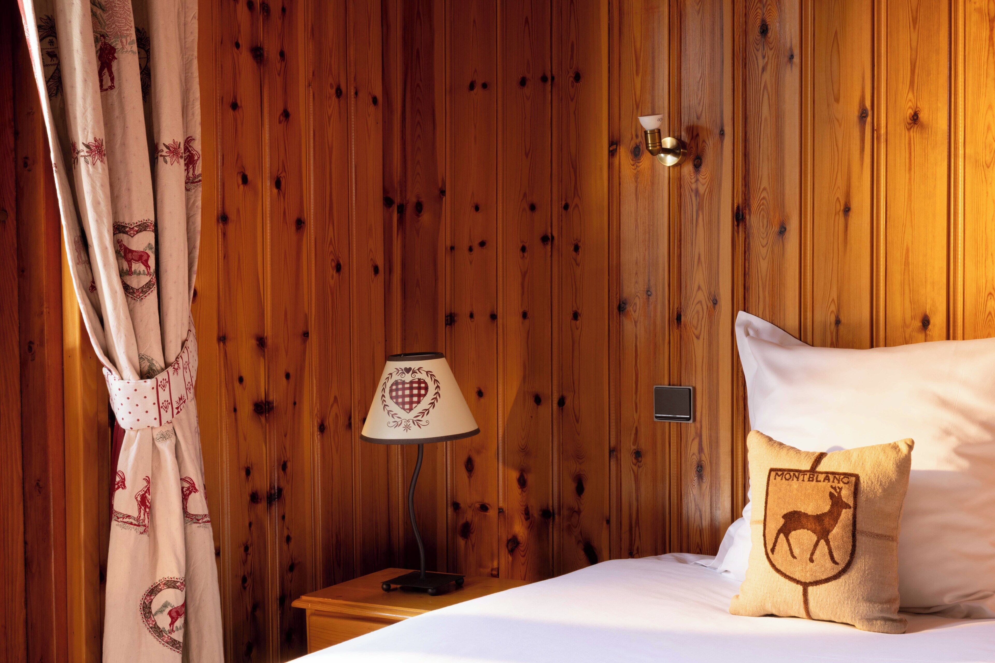 A wooden-paneled room with a bed, a nightstand, a lamp, and a decorative pillow.