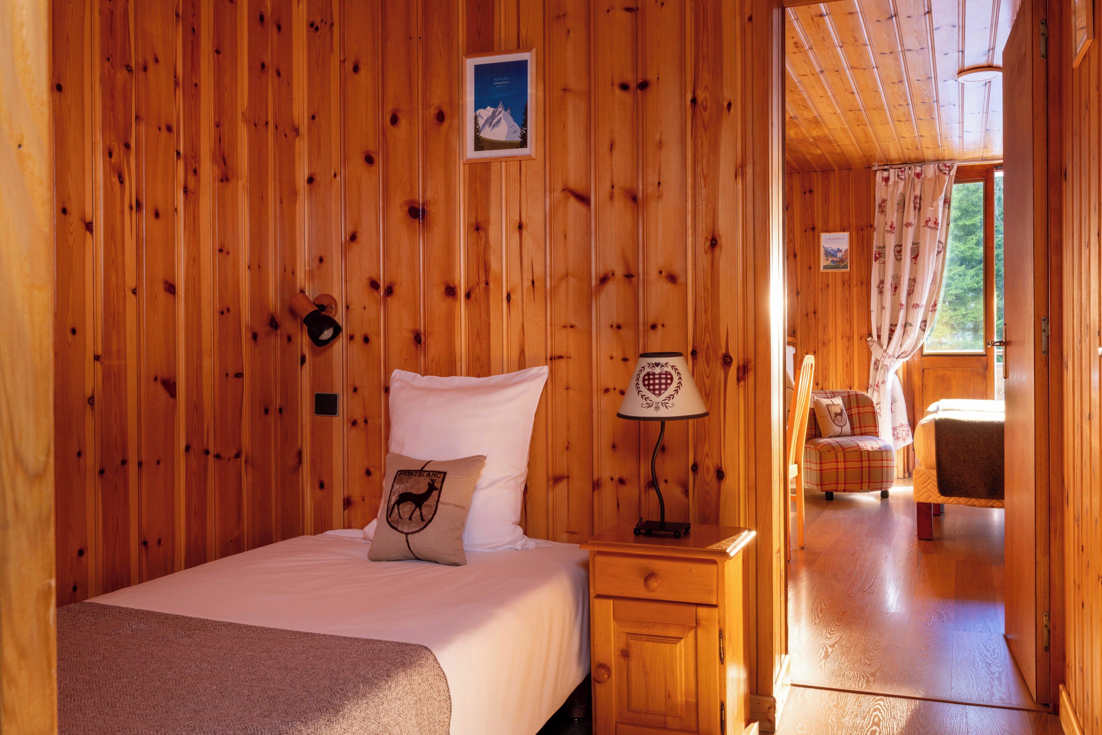 Een kamer met houten lambrisering, een bed, nachtkastje, lamp en stoel.