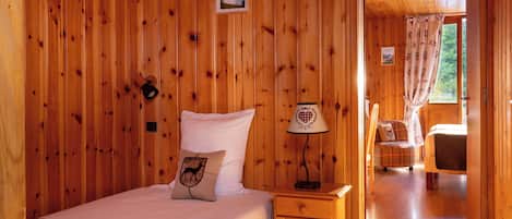 A wooden-paneled room with a bed, a nightstand, a lamp, and a chair.