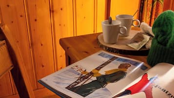 Una revista sobre una mesa de madera con dos tazas blancas y una cuchara, un peluche verde y una silla de madera.
