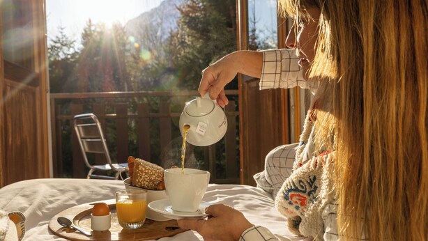 A person pouring a beverage into a cup on a table with a tray of food and a glass of juice. - L’Arveyron Open House (Chamonix-Mont-Blanc)