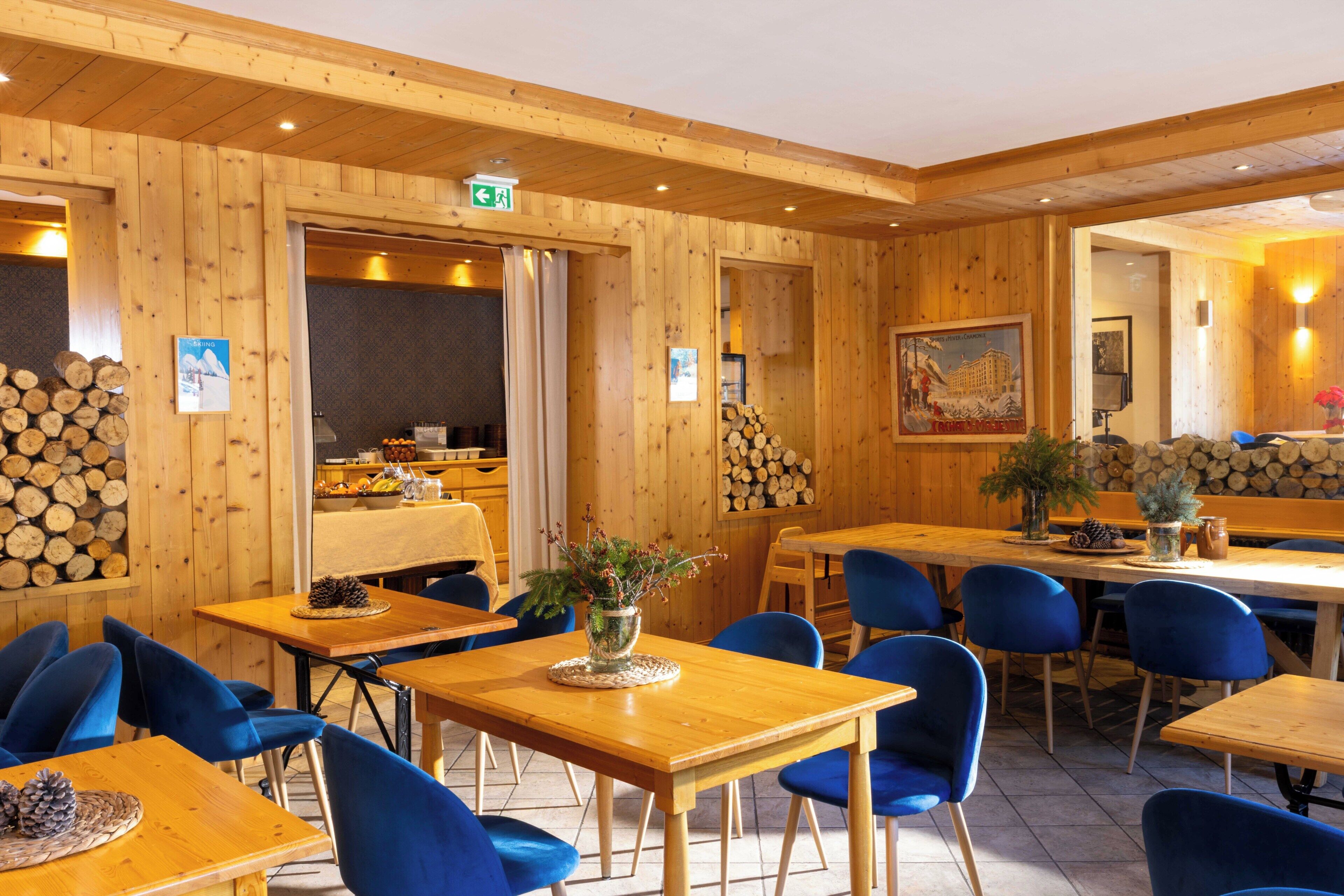 A wooden interior with tables and blue chairs, a framed picture on the wall, and a log display.