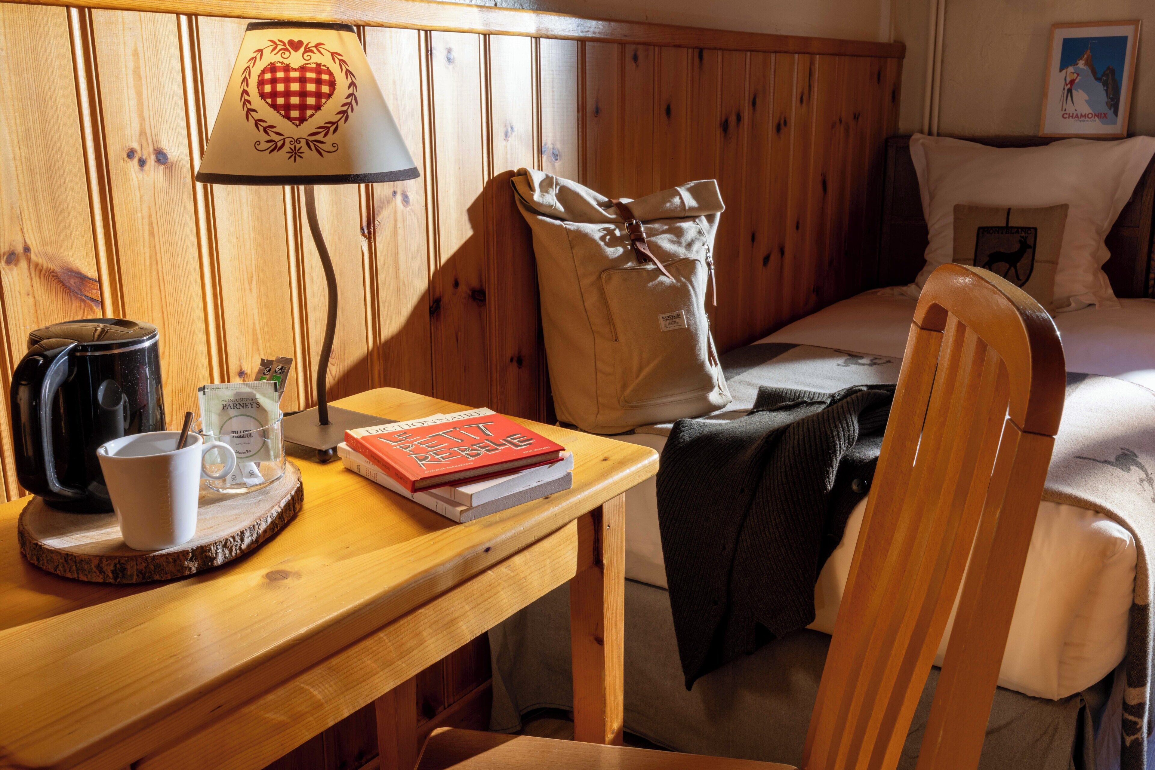 Une pièce en bois avec un lit, une table sur laquelle se trouve une lampe, une tasse et un livre.
