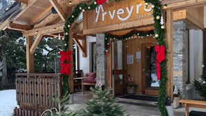 A wooden building with a sign reading "Arveyo Open H." It features a wooden porch, a small Christmas tree, and snow on the ground. - L’Arveyron Open House (Chamonix-Mont-Blanc)