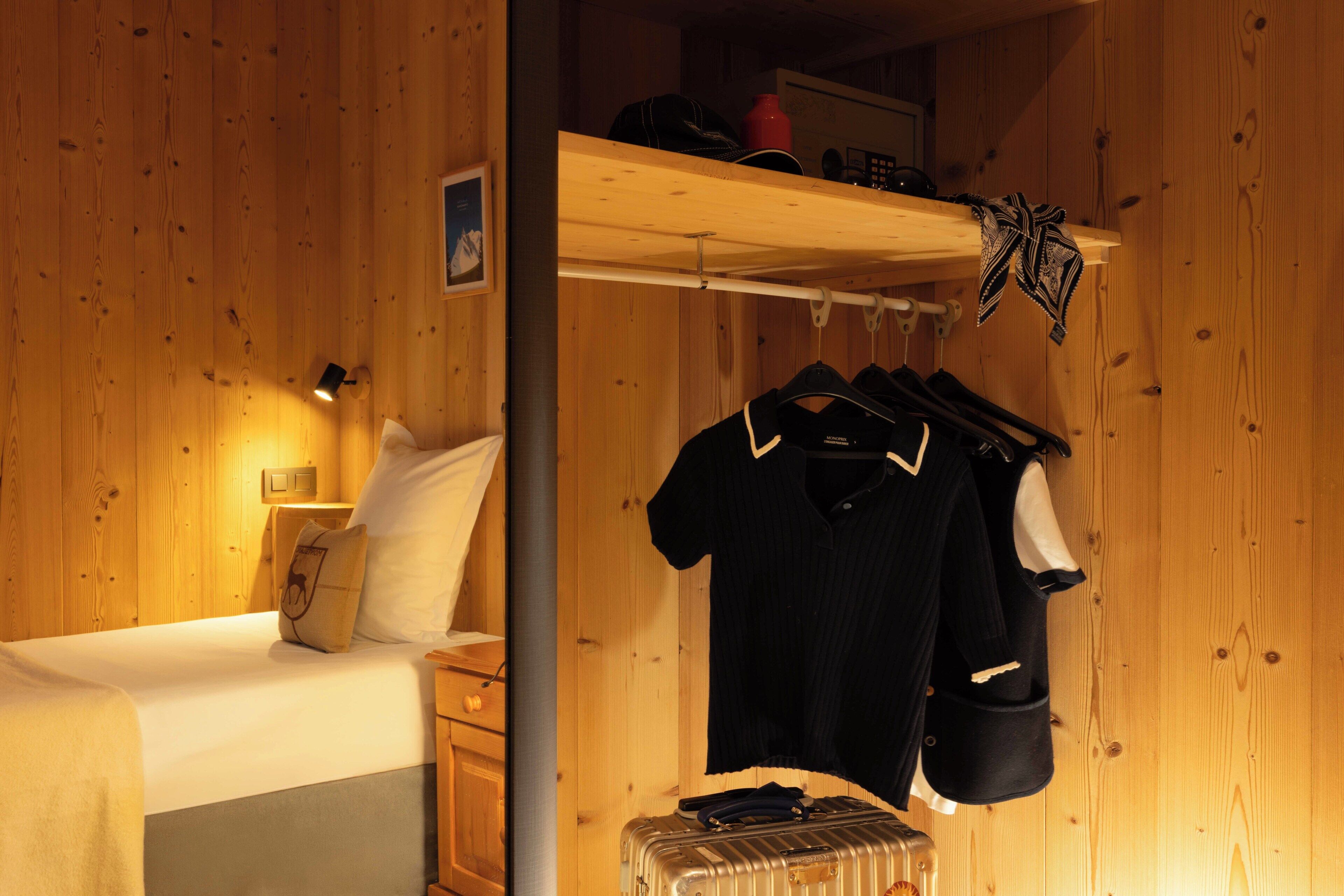 A wooden room with a bed, a hanging coat rack, and a suitcase.