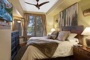 A bedroom with a bed, a ceiling fan, a painting, a window with curtains, and a dresser.
