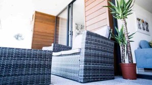 A corner of a room with a wicker sofa, a potted plant, and a wooden door. - No2 Sandy Bay , Luxury Beachfront Apartment (Portrush)