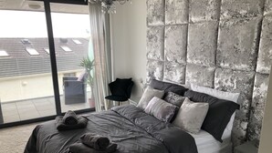 A modern bedroom with a large bed, a nightstand, a chair, and a view of the outside. - No2 Sandy Bay , Luxury Beachfront Apartment (Portrush)