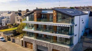 A modern two-story building with a glass facade, a stone base, and a flat roof. - No2 Sandy Bay , Luxury Beachfront Apartment (Portrush)