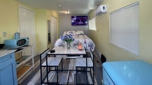 A compact room with a bed, a small table with chairs, a microwave, and a TV on the wall.