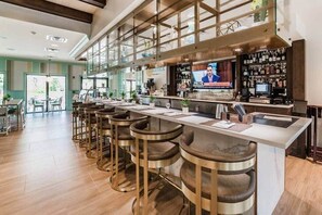Zona de bar amb un taulell llarg, diverses banquettes, una pantalla de televisió i una barra plena de garrafes.