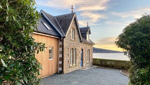 A stone building with a sloped roof, a wooden door, and a gravel driveway. - Greenlea -Scenic loch-side location, coastal retreat boasts spectacular sea views, sleeps 4 (Strachur)
