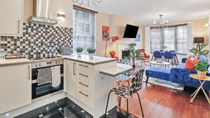 A modern kitchen with a central island, a dining area with a blue sofa, and a living room with a TV and a chandelier. - Central Lanes Pad | By My Getaways | Free parking for one car (Brighton)