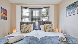 A double bed with a grey duvet and white pillows, a window with blinds, and a painting on the wall. - Central Lanes Pad | By My Getaways | Free parking for one car (Brighton)