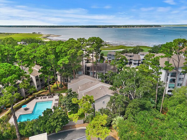 A residential area with a swimming pool, surrounded by trees and a view of a large body of water.