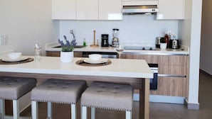 A modern kitchen with white cabinets, a central island with bar stools, and various appliances.