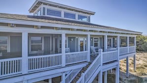 A coastal house with a covered porch, multiple windows, and a staircase leading to an upper level.