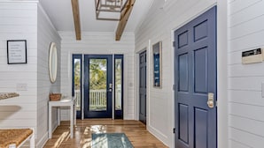 A hallway with wooden floors, a blue door, and a white wall with a framed quote.