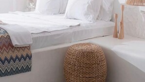 A modern bedroom with a bed, bedside lamps, a woven ottoman, and a patterned throw blanket.