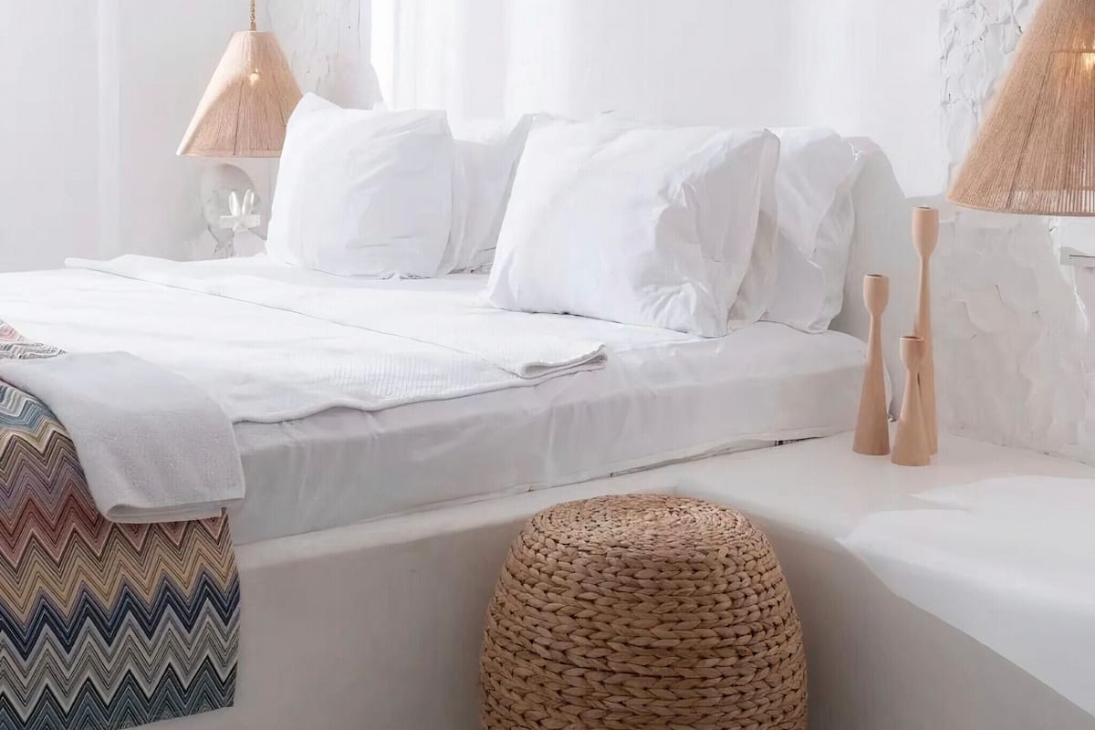 Un dormitorio moderno con cama, lámparas de noche, un otoman tejido y una manta estampada.