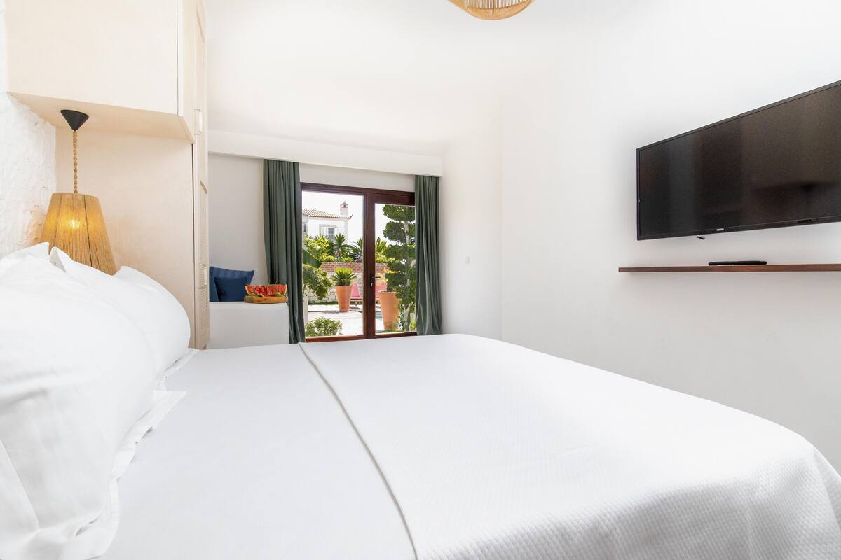 Habitación de hotel con una cama grande, un televisor montado en la pared y vistas al exterior a través de una ventana.