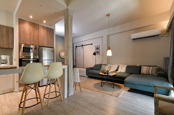 A modern kitchen with built-in appliances, a dining area with chairs, a sofa, and a small table with a lamp. - Discover Athens from an Upscale flat in Koukaki! (Αθήνα)