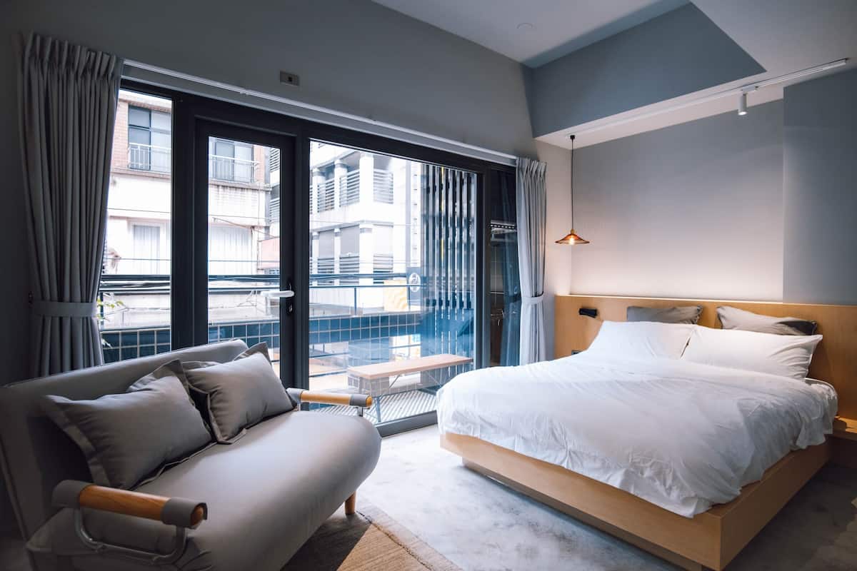 Una habitación de hotel moderna con una cama grande, un sofá y un balcón con vistas a la ciudad.