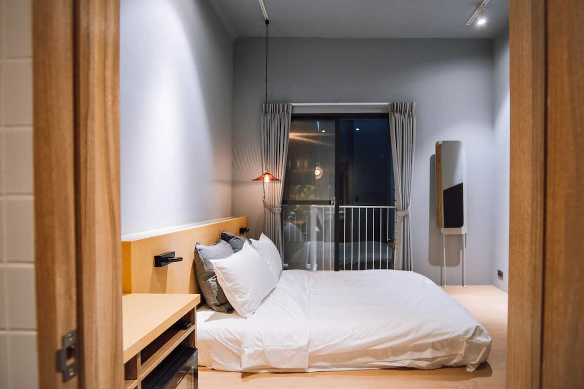 Un dormitorio moderno con cama, mesita de noche y ventana con cortinas.
