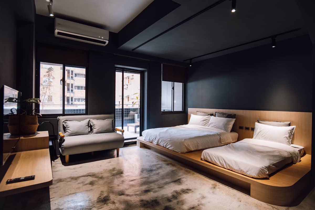 Un hotel moderno con una cama grande, un sofá, un escritorio y vistas de la ciudad a través de amplias ventanas.