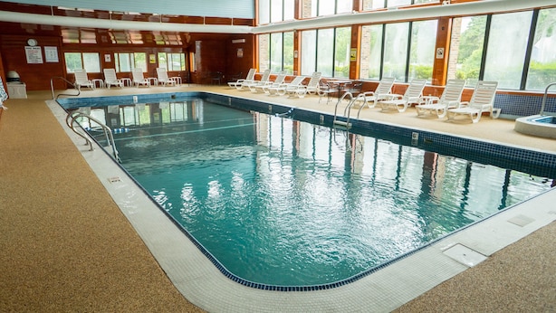 Una piscina interior con agua cristalina, rodeada de sillones de descanso y un solárium con baldosas.