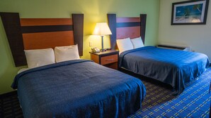 Una habitación de hotel con dos camas, una mesita de noche con lámpara y un cuadro en la pared.