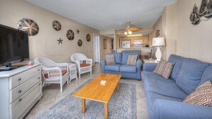 A living room with a TV, white wicker furniture, a blue sofa, and a wooden coffee table. - Bluewater Resort 901 - 2 Bedroom/Bath Ocean View Condo, Indoor/Outdoor Pool, Hot tub (Myrtle Beach)