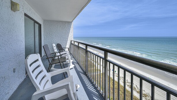 Een balkon met witte kunststof stoelen en uitzicht op de oceaan.