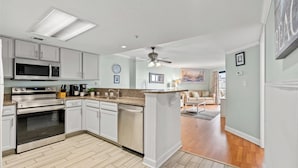 A modern kitchen with white cabinets, stainless steel appliances, and a wooden floor.