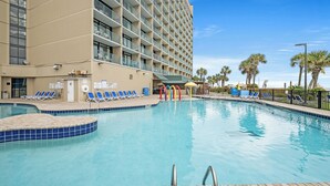 A hotel pool area with a large pool, lounge chairs, and a building with multiple balconies.