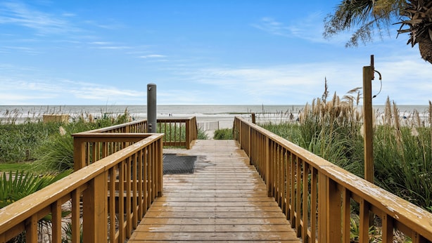 A wooden boardwalk leading to a beach with a clear sky.