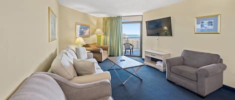 Habitación de hotel con sala de estar que incluye un conjunto de sofás, una mesita de centro, un televisor y un balcón con vistas.