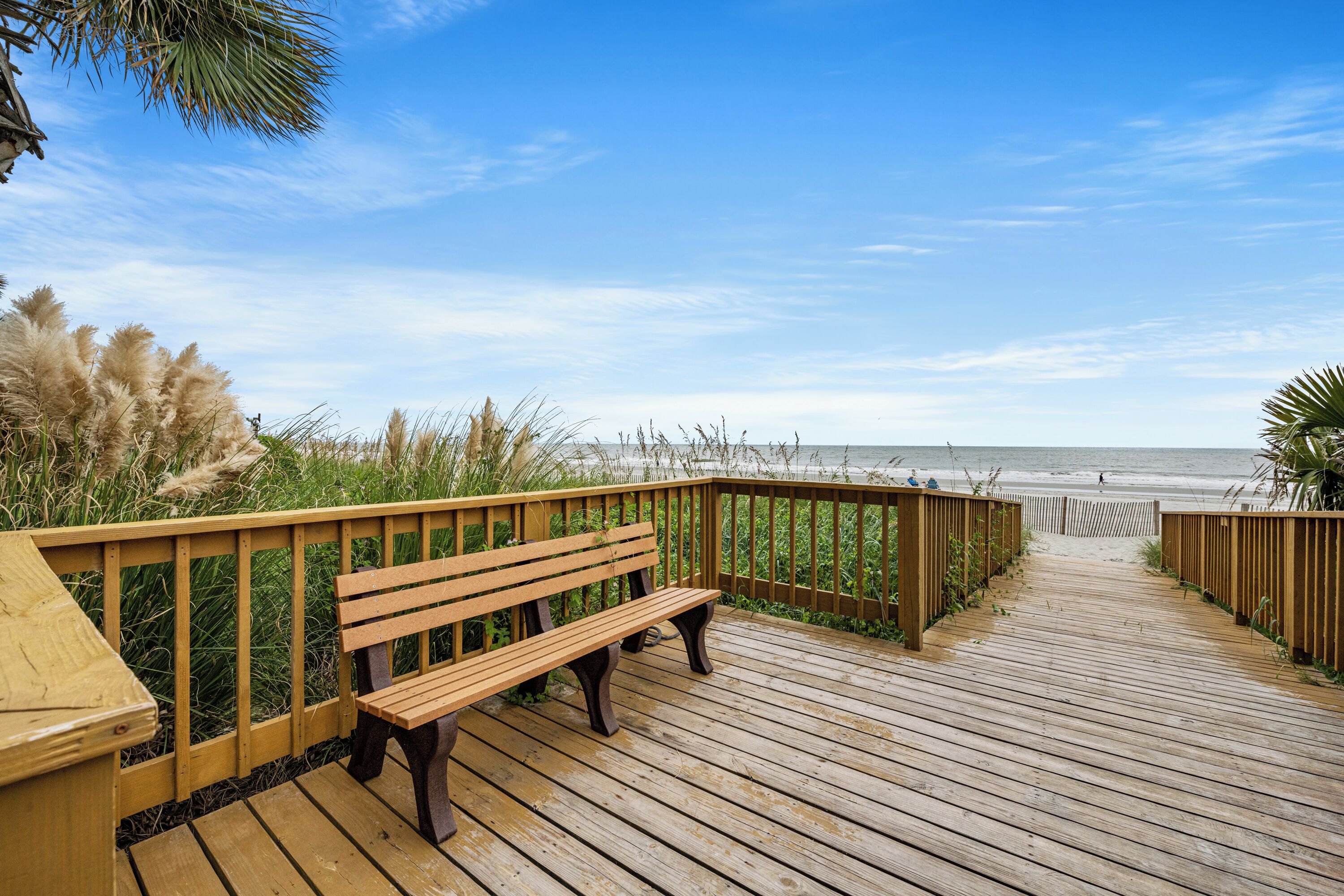 Une promenade en bois menant à une plage, avec un banc et une rambarde.