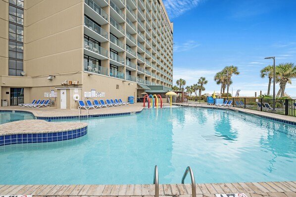 A hotel with a swimming pool, multiple balconies, and palm trees.