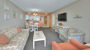 A living room with a sofa, a coffee table, and a television. There is a kitchen area in the background with a dining table and chairs. - SAND DUNES SOUTH TOWER 1150 AND 1149 (Myrtle Beach)