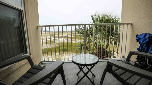 Un balcon avec une table et deux chaises, donnant sur un espace verdoyant et agrémenté d’un palmier.