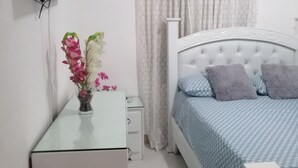 A bedroom with a bed, a bedside table, a TV mounted on the wall, and a vase with flowers on the table.