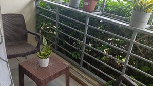 A balcony with wicker chairs, a small table with a potted plant, and a metal railing with potted plants.