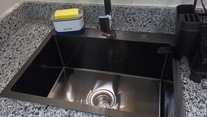 A kitchen with a stainless steel sink, a soap pump, and a window with floral curtains.