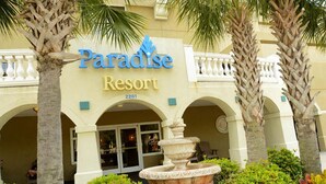 The Paradise Resort building with a sign, palm trees, and a fountain.
